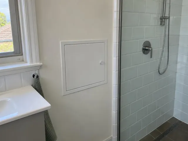 Bathroom wall with a small access panel beside a shower and sink in Hornsby